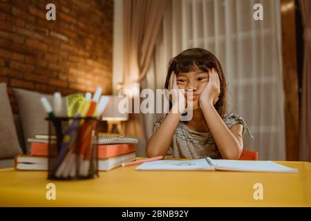 kid feel bored while doing her homework at home in the evening Stock Photo