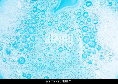 Close-up White Foam with bubbles on surface of water, washing powder with soap and blue bath, abstract background transparent bubble. Stock Photo