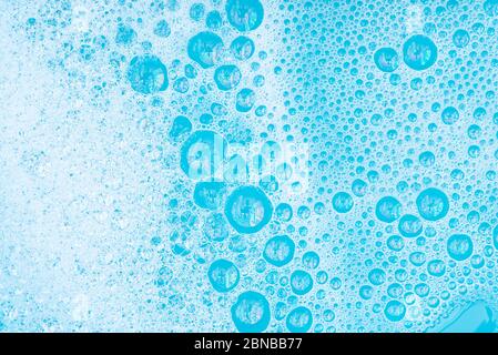 Close-up White Foam with bubbles on surface of water, washing powder with soap and blue bath, abstract background transparent bubble. Stock Photo
