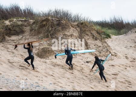 Young Female surfers carrying their surfboards and climbing up the sand dunes after surfing at Fistral in Newquay in Cornwall. Stock Photo