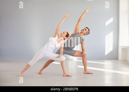 Yoga for health. A man and a woman in sportswear are practicing yoga in a bright classroom. The couple is doing exercises on the floor. The concept of Stock Photo