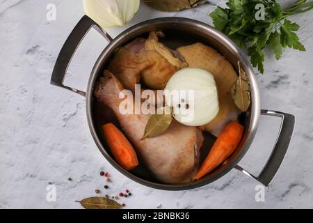Cooking broth from homemade chicken with pepper and bay leaf in a pan on a marble background. Vegetables are added to the broth: onions and carrots Stock Photo