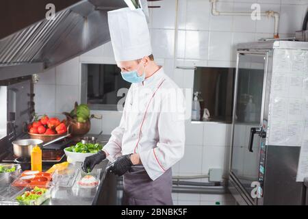 Cooking in a restaurant by a cook in a medical mask and packing in a container Stock Photo