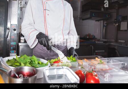 Cooking in a restaurant by a cook in a medical mask and packing in a container Stock Photo