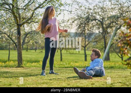 Young couple on a meadow between apple trees in spring laughing happily at each other and having fun Stock Photo