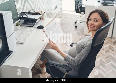Smiling pregnant lady working in modern office Stock Photo