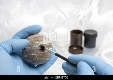 A human hand in blue protective gloves painting the planet Venus on a styrofoam ball and in the background there are paints of black, brown and white. Stock Photo