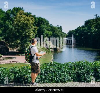 Sofia Park, Ukraine. Man with a backpack with a tourist map in a landscape park in summer. Guy in a T-shirt with a tourist map on the background of th Stock Photo