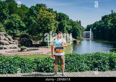 Sofia Park, Ukraine. Handsome man with a beard in a dendrological park. Man with a backpack on the background of the lake with a fountain and a white Stock Photo