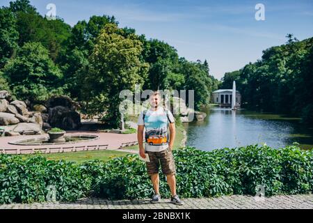 Sofia Park, Ukraine. Handsome man with a beard in a dendrological park. Man with a backpack on the background of the lake with a fountain and a white Stock Photo