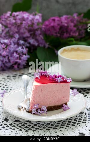 A berry mousse cake with chocolate base and juice jelly, decorated with lilac flowers, served with coffee. Stock Photo
