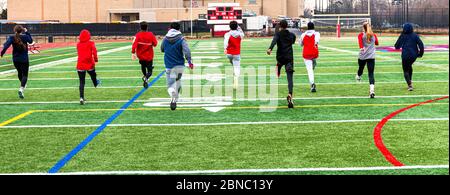 Rear view of high school track team of boys and girls performing warm up running drils side by side on a greeen turf field. Stock Photo