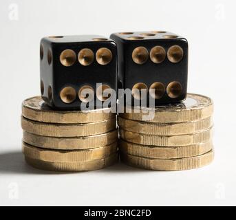 Two black dice on stacks of one pound coins against a white background gambling concept Stock Photo
