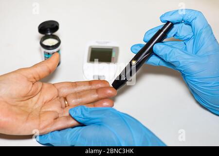 Nurse taking blood sample from a patient using a Glucometer to measure blood sugar level of a patient Stock Photo