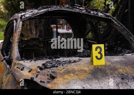 Dresden, Germany. 13th May, 2020. On the bonnet of a burnt-out car there is a yellow forensic plaque of the criminal investigation department with the number three. The destroyed vehicle is visible in the blurred background of the picture. Credit: Tino Plunert/dpa-Zentralbild/ZB/dpa/Alamy Live News Stock Photo
