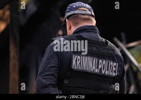 Dresden, Germany. 13th May, 2020. Police officer with the inscription Kriminalpolizei on his back is in the middle of the picture. In the blurred background of the picture, burnt wooden beams can be seen. Credit: Tino Plunert/dpa-Zentralbild/ZB/dpa/Alamy Live News Stock Photo