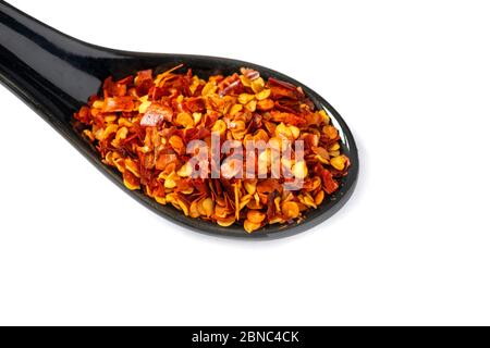From above ceramic spoon with heap of dried red hot chili pepper isolated on white background Stock Photo