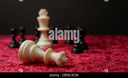 White king surrounded by black pawns and fallen white queen Stock Photo