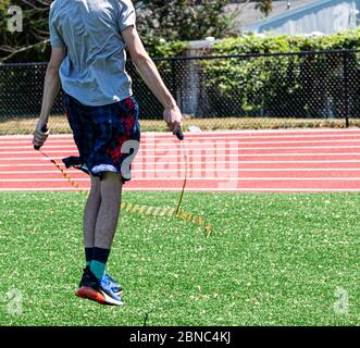 Rear view of a teenage track runner jumping rope during practice on a green turf field. Stock Photo