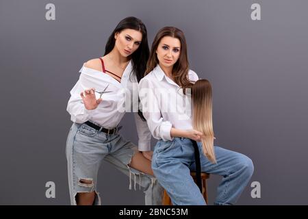 Fashion portrait of two Professional hairdressers. Two hair stylists or artists holding sections of hair for extension or hair tresses and scissors Stock Photo