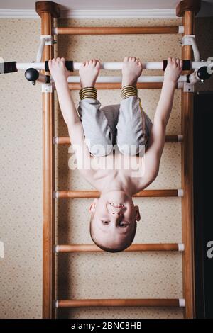 Home workout. The boy hangs head down on the horizontal bar. Stock Photo