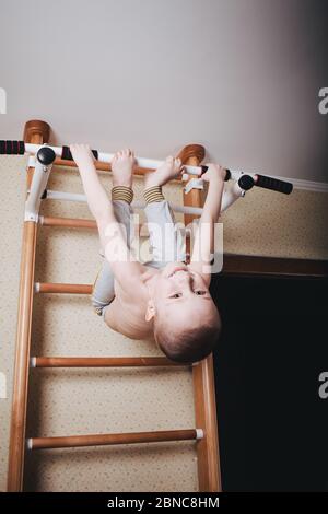 Home workout. The boy hangs head down on the horizontal bar. Stock Photo