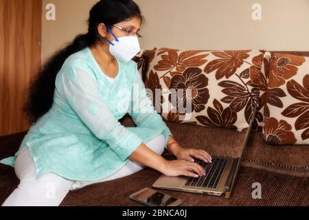 Indian woman in protective face mask work from home during coronavirus lock down Stock Photo