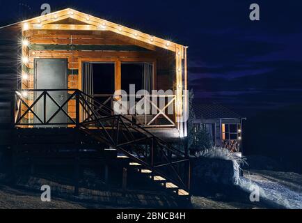 Modern wooden house decorated with yellow glowing bulbs at the mountain resort Stock Photo
