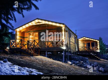 Modern wooden houses decorated with yellow glowing bulbs at the mountain resort Stock Photo