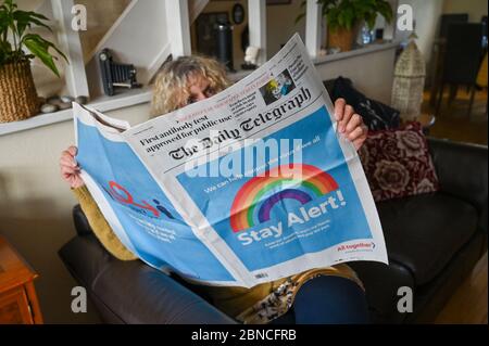 Brighton UK 14th May 2020 - A Brighton resident reads the Daily Telegraph which carries the governments 'Stay Alert' campaign message on the front page after lockdown measures had been relaxed slightly in England from yesterday during Coronavirus COVID-19 pandemic crisis  . Credit: Simon Dack / Alamy Live News Stock Photo