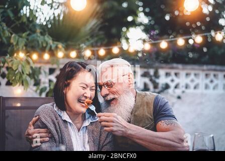 Happy senior couple having fun at dinner house party - Older people with different ethnicity doing a romantic date for celebrating anniversary Stock Photo