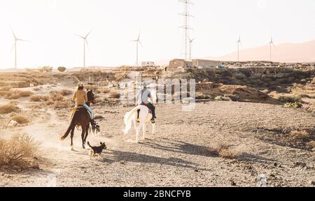 Young people riding horses in desert - Horseback travel people having fun exploring wild nature - Animals passion and equestrian lifestyle concept Stock Photo