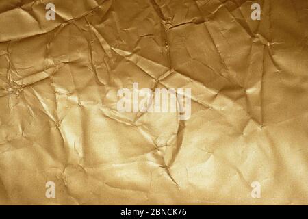 Texture of golden crumpled paper. Background fabric of gold color, creases. Crumpled gold-plated gift wrapping paper. Stock Photo