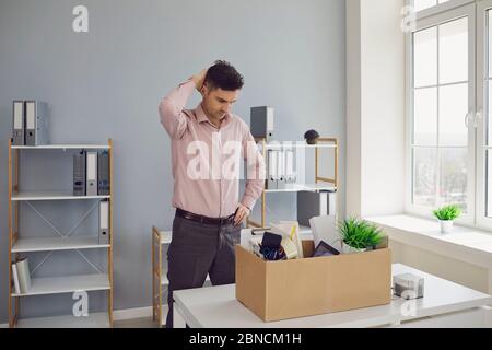 Unemployment. Dismissal. Dismissed businessman is upset with a cardboard box holding his head in his hands while sitting at a table in the company off Stock Photo