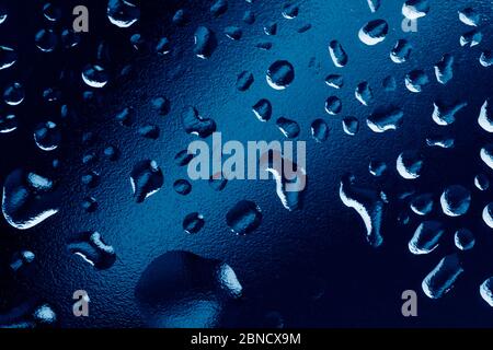 Water drops on window glass. Rain drops on dark trendy blue background. Macro, closeup. Stock Photo