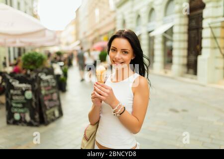 Beautiful girl with gelato smiling on sunny street. Young pretty woman having fun and eating ice cream in front of market street in historical part of Stock Photo