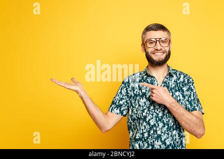 smiling bearded guy in glasses pointing with finger aside on yellow Stock Photo