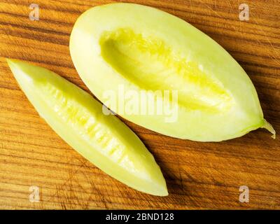 Half of a canary melon with one slice cut away on a wooden chopping board Stock Photo