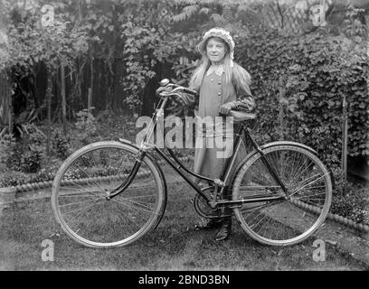 A vintage late Victorian or early Edwardian black and white photograph, taken in England, showing a young girl with a new loop frame ladies bicycle. The photograph is taken in the garden of a house. Girl is wearing nice fashionable clothes, with a bonnet and leather gloves. Stock Photo