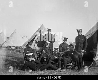 Vintage late Victorian photographs, taken in 1903,  showing members of the 2nd London Rifles, or the 2nd City Of London Rifle Volunteer Corps. It is unsure if these photographs were taken in England or South Africa, where many of the Volunteers were based at this time. Photo shows a group of nine officers and soldiers sitting and standing outside a row of canvas tents. Stock Photo