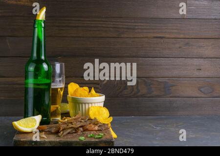 Dried carp fish sticks with beer, lemon and potato chips on dark wooden board. Snack on fish with beer. Front views with clear space Stock Photo