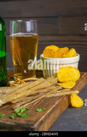 Dried salted tuna elite snack with beer, lemon and potato chips on dark wooden board. Snack on fish with beer. Front views, close-up Stock Photo
