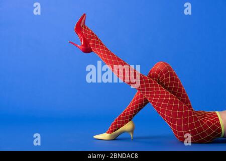 cropped view of woman in fishnet tights and red heels posing on