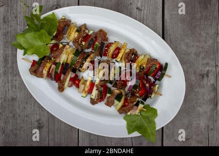 Skewer before grilling composed of bacon onions tomatoes meat pork zucchini peppers on a plate with leaves on a wooden table Stock Photo
