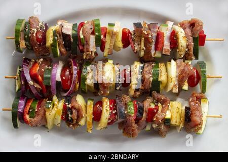 Skewer before grilling composed of bacon onions tomatoes meat pork zucchini peppers on a white plate Stock Photo