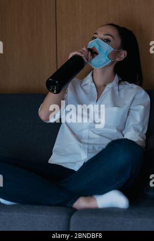 depressed woman in medical mask with hole drinking wine from bottle