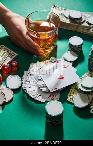 KYIV, UKRAINE - MARCH 2, 2020: cropped view of woman holding glass of cognac near money, playing cards, dice and casino tokens on green Stock Photo