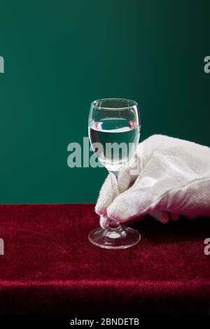 Cropped view of hand in terry glove holding shot glass with liquid isolated on green Stock Photo