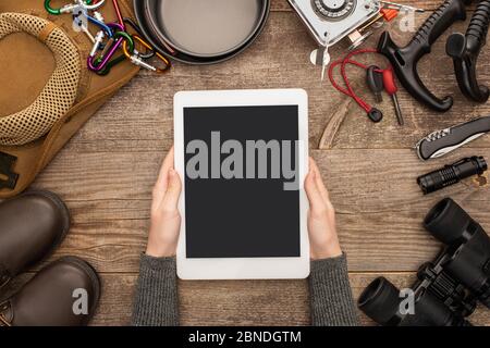 partial view of woman holding tablet with blank screen over hiking equipment on wooden table Stock Photo