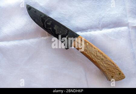 The bladesmith put a lot of love and care into the construction of this hand forged damascus knife with wooden handle. Bokeh. Stock Photo